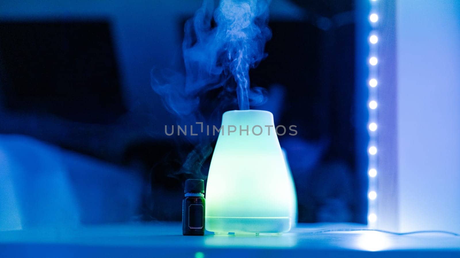One electric air freshener with a bottle of aromatic oil lie on a table in a home beauty salon in neon light with evaporating steam, close-up side view with selective focus.