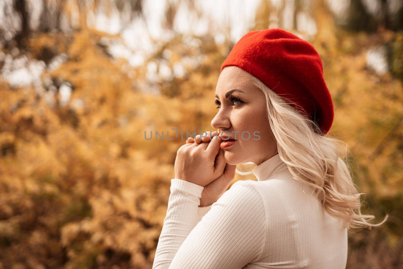 A blonde woman wearing a red hat and a white shirt is standing in a forest. She is looking at the camera with a serious expression