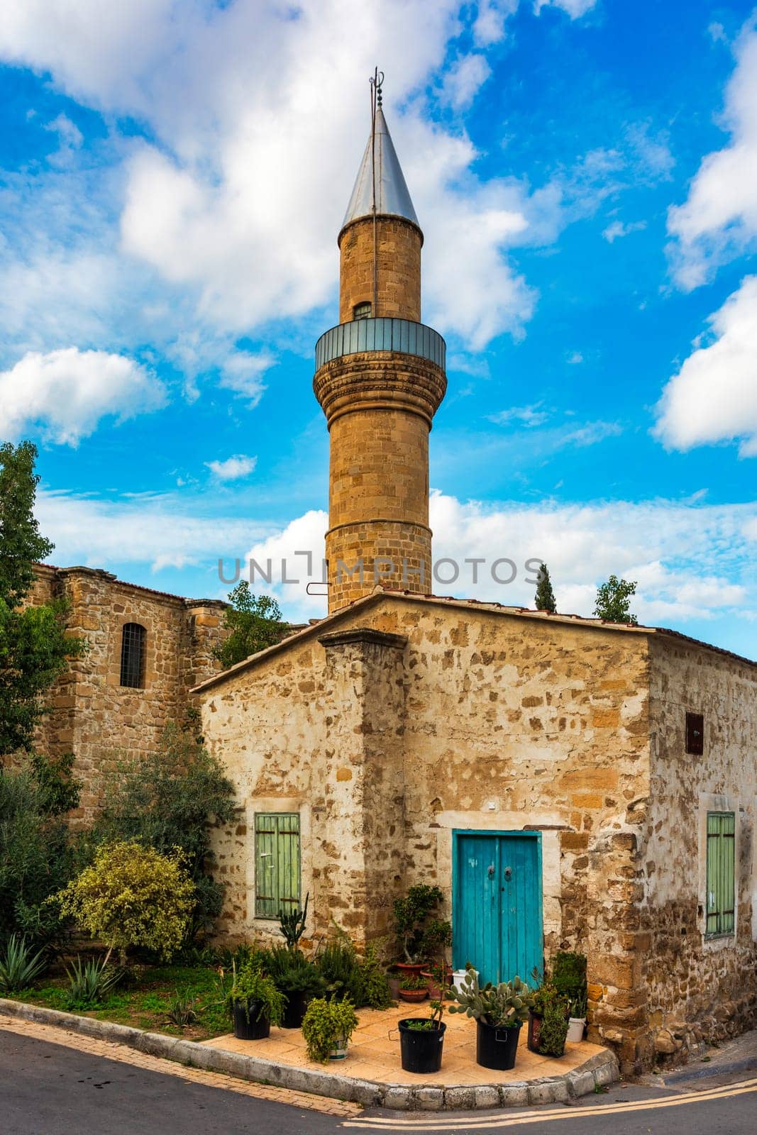 A small building with a blue door sits in front of a large Mosque with a tall tower in Nicosia, Cyprus. Beautiful street with old architecture in Nicosia, Cyprus.