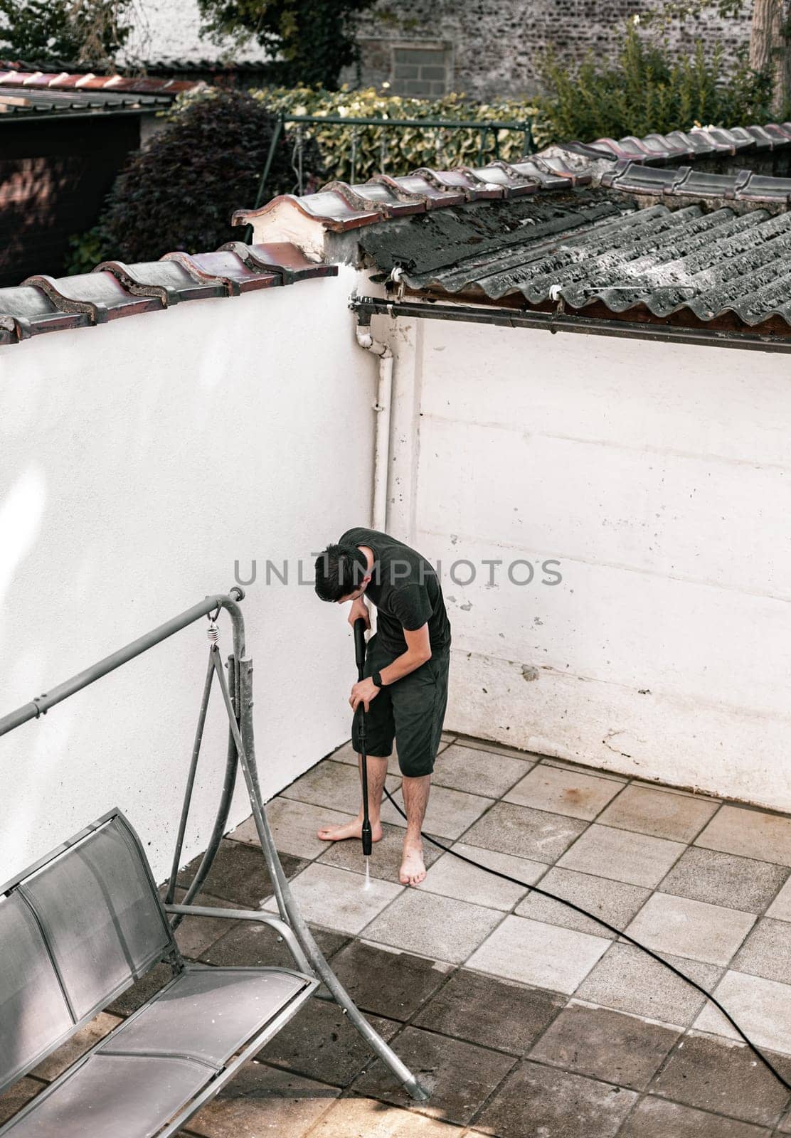 A young guy washes his backyard with a kercher. by Nataliya