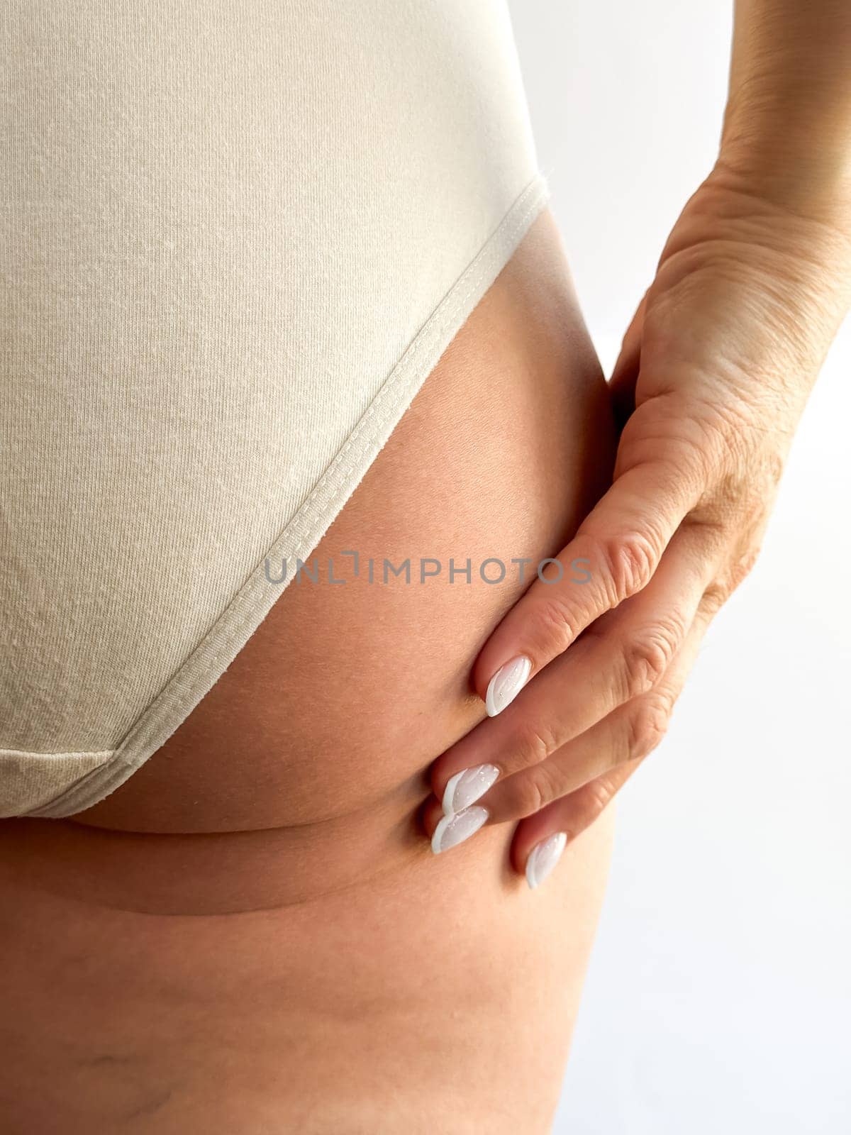 Close up of womans hand with white nails resting on hip, wearing beige underwear. Focuses on skincare, body care, and personal hygiene, highlighting healthy skin and well groomed nails. High quality