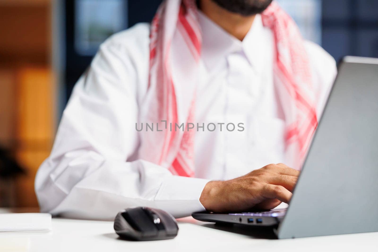 Detailed view of an Arab person utilizing modern technology by typing on a wireless computer. Close-up shot of a digital laptop being used by a young adult in Arabic clothing.