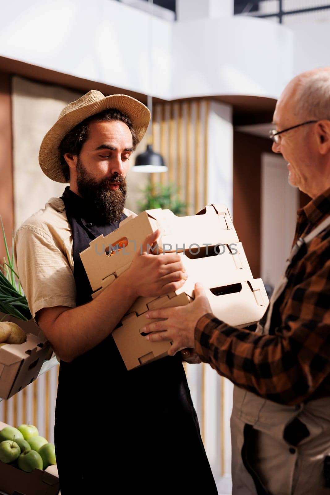 Old farmer providing locally sourced bio vegetables to seller selling it to environmentally conscious customers in zero waste shop. Aged man handing crates full of pesticides free produce to retailer