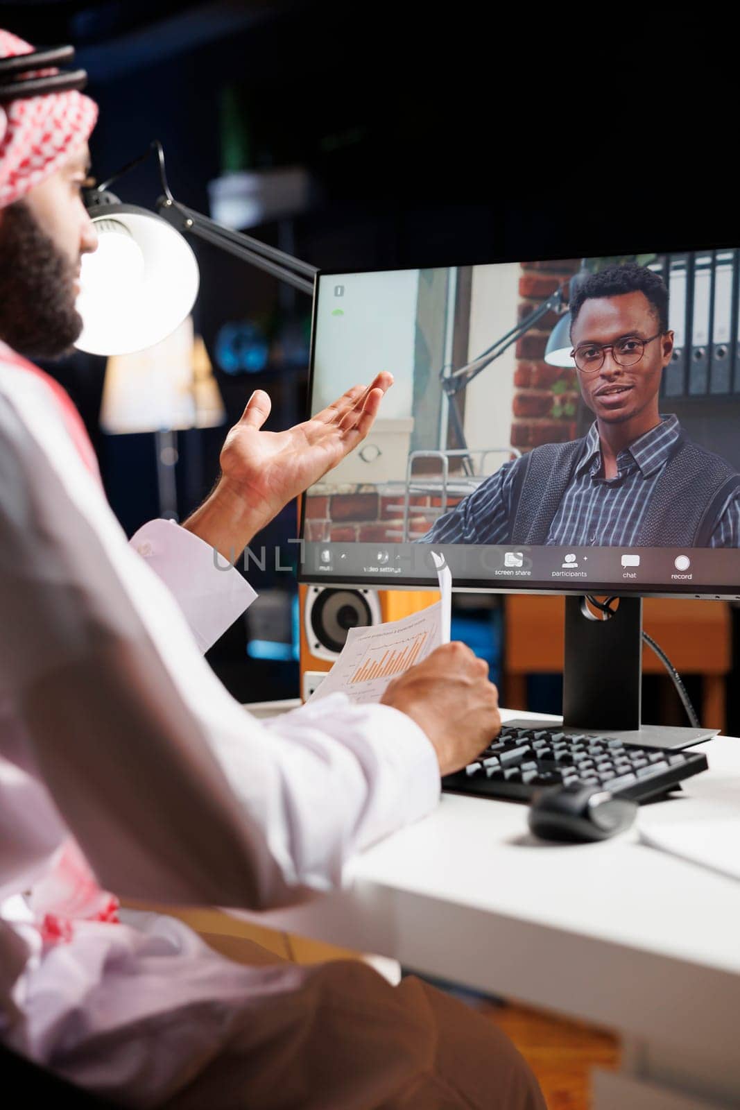 Video call is prominently featured on computer screen, showing conversation between Muslim freelancer and African-American colleague. Image underscores use of modern technology by young individuals.