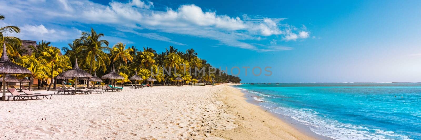 A beach with palm trees and umbrellas on Le morne Brabant beach in Mauriutius. Tropical crystal ocean with Le Morne beach and luxury beach in Mauritius. Le Morne beach with palm trees, white sand and luxury resorts, Mauritius.