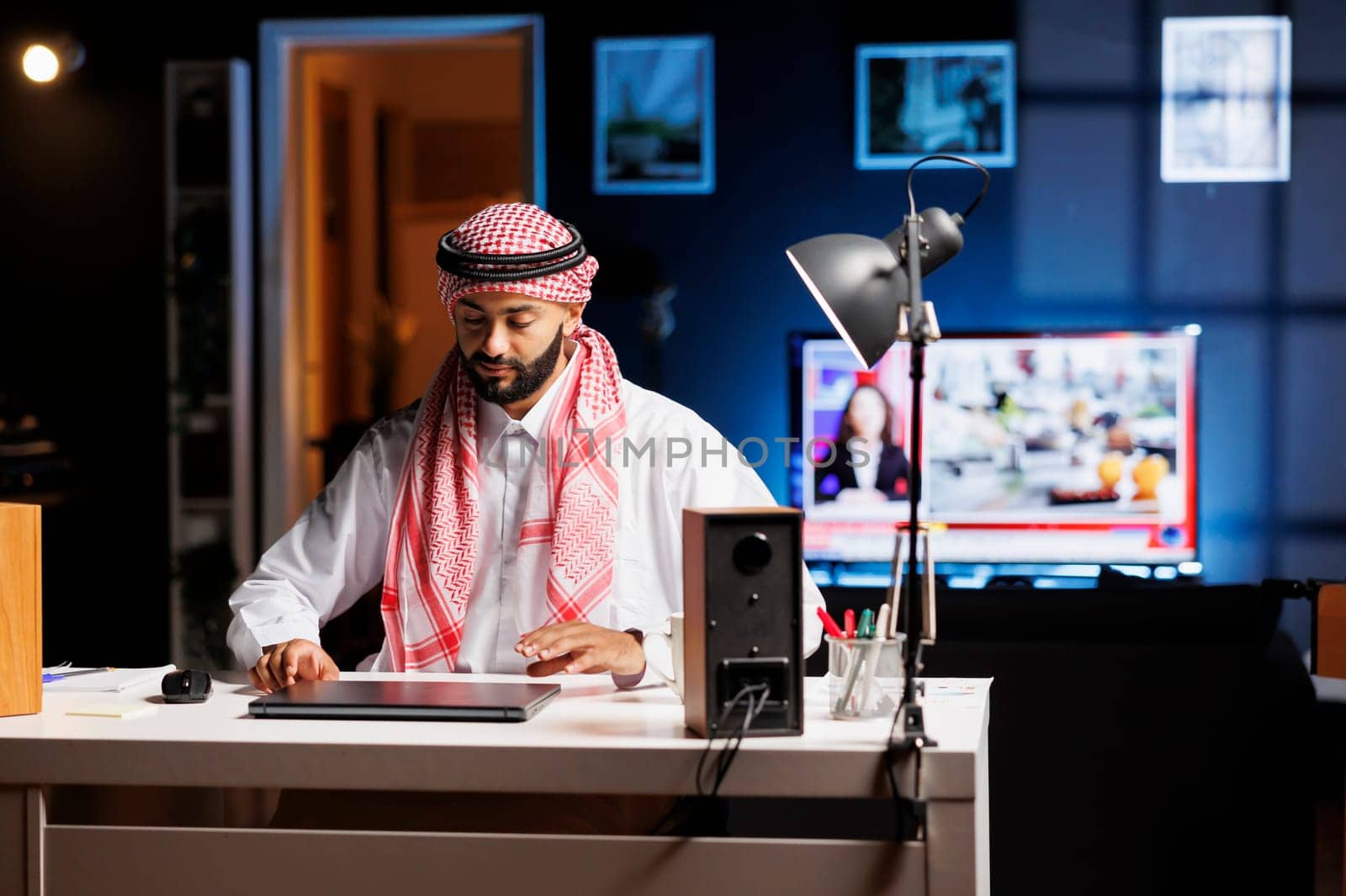 Middle Eastern man in Arabic clothing sitting at the table with his digital laptop preparing for work. Dedicated Muslim man is about to open his wireless computer for browsing the internet.