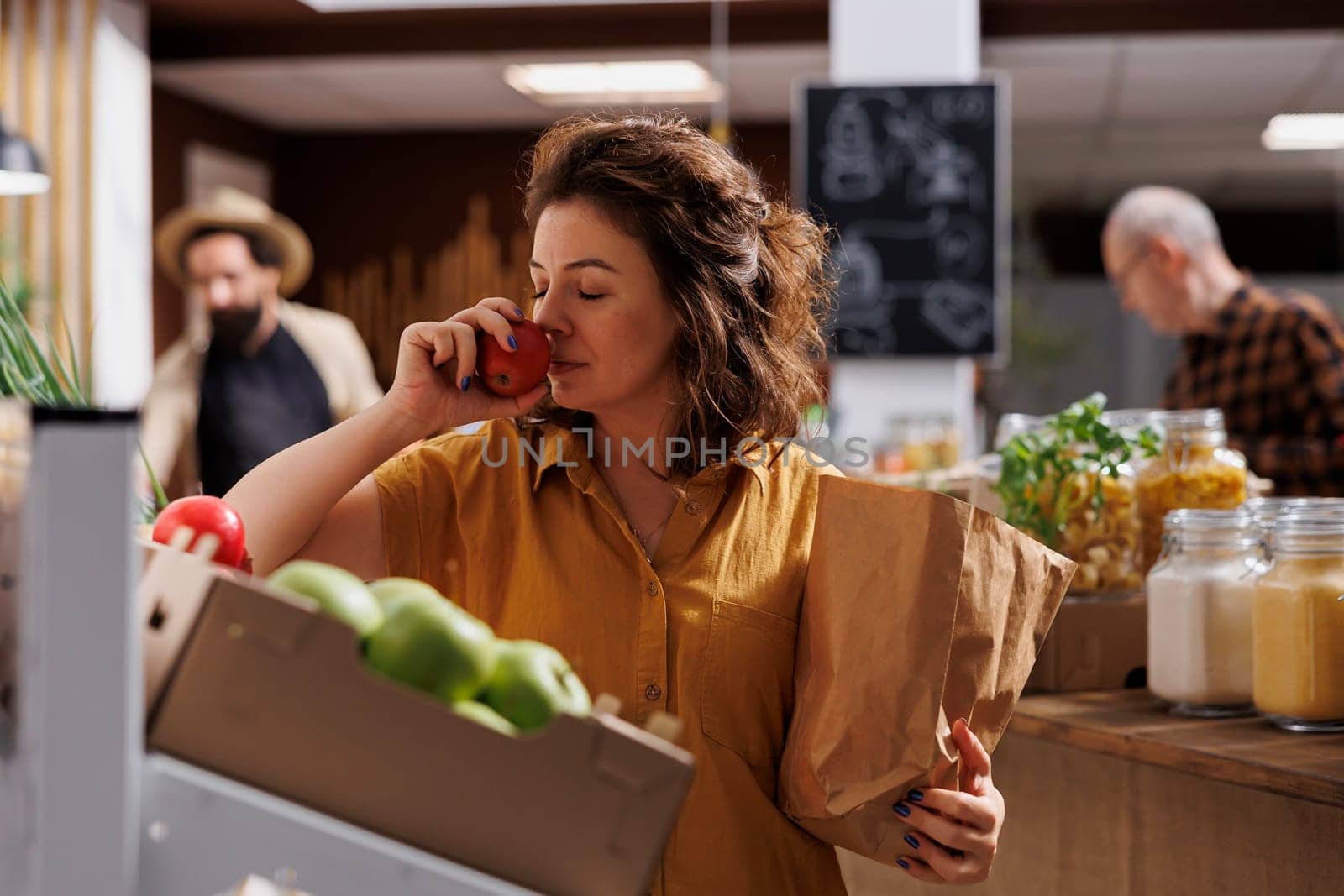 Woman smelling bio apples in supermarket by DCStudio