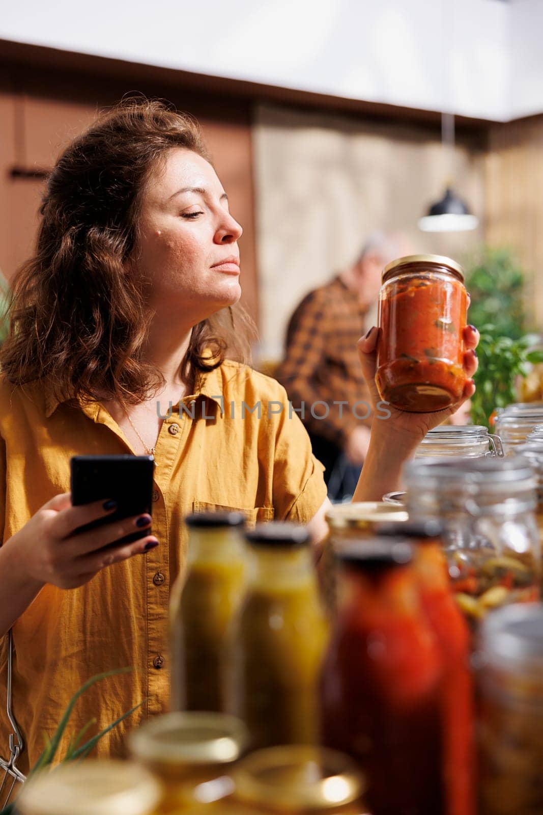 Healthy living woman in zero waste store using smartphone notes app to check shopping list. Meticulous customer looking to replenish pantry at home with natural pesticides free food essentials