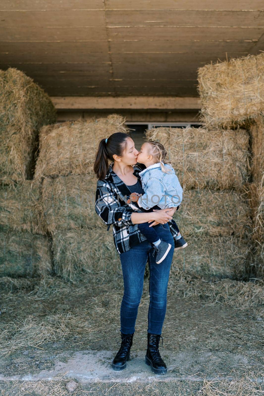 Mom kisses a little girl in her arms standing in the hayloft. High quality photo
