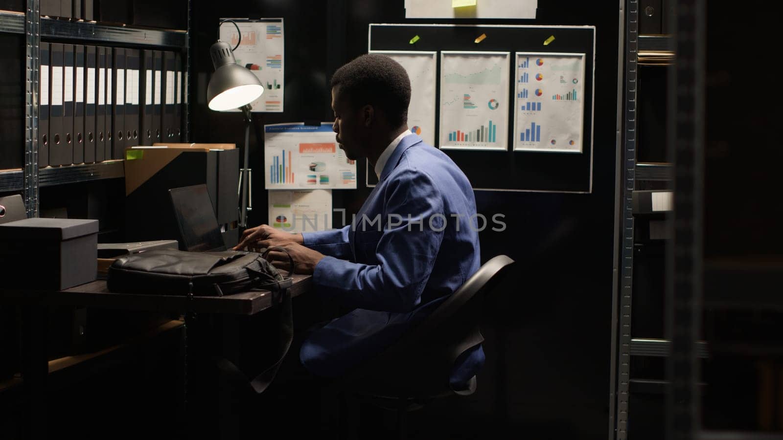 Arriving at workplace, black man with experience in criminal investigation opening his minicomputer. African american investigator sitting in workroom with laptop bag, ready to conduct study.