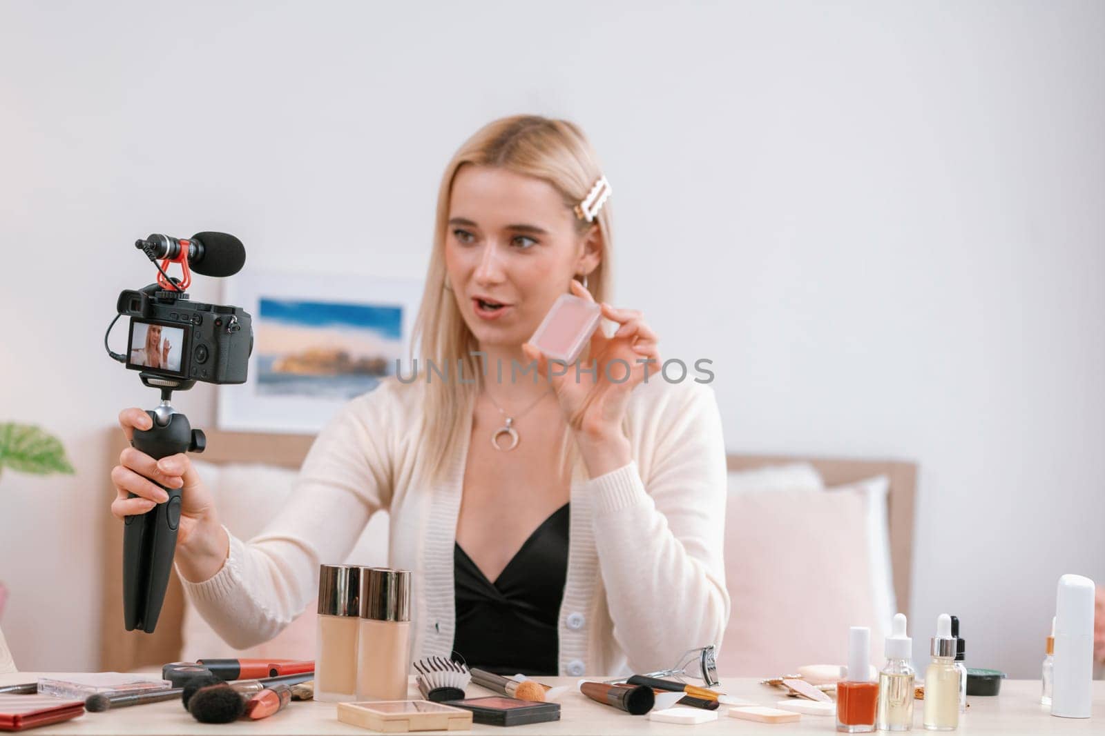 Young woman making beauty and cosmetic tutorial video content for social media. Beauty blogger smiles to camera while showing how to beauty care to audience or followers. Blithe