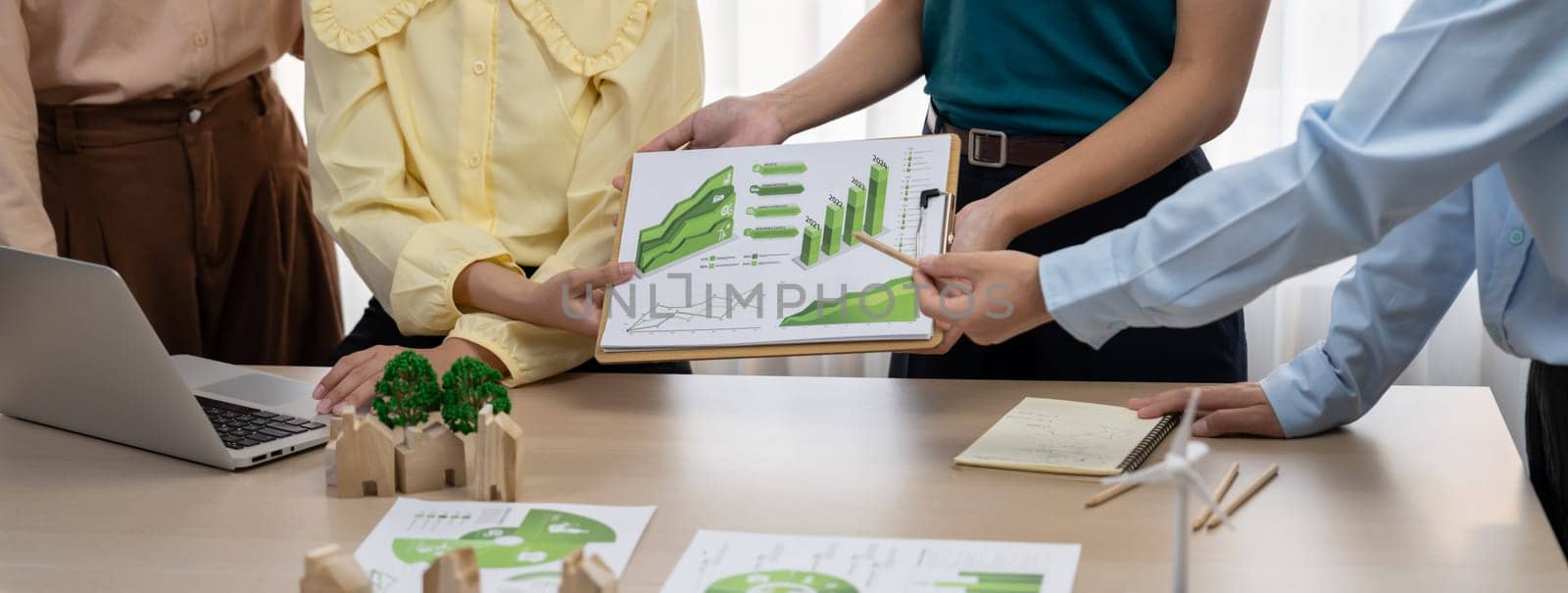 Professional business team presenting green business project by using graph to explain benefit of using renewable energy at modern meeting room. Closeup. Focus on hand. Delineation.