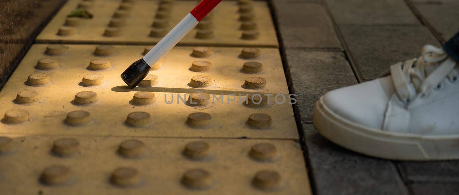 A close-up of a woman's feet with a tactile cane and a tactile tile indicating an obstacle. by mrwed54