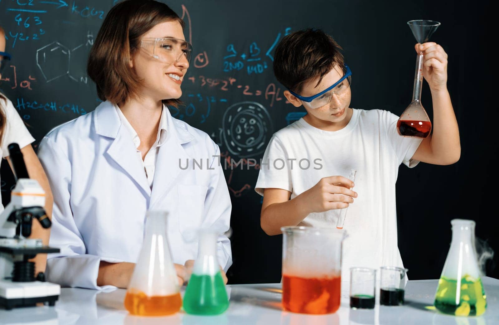 Teacher in support and watch student in laboratory they wear safety glasses, stand and experiment about science of chemistry in STEM class. Student funny do experiment with liquid in tube. Erudition.