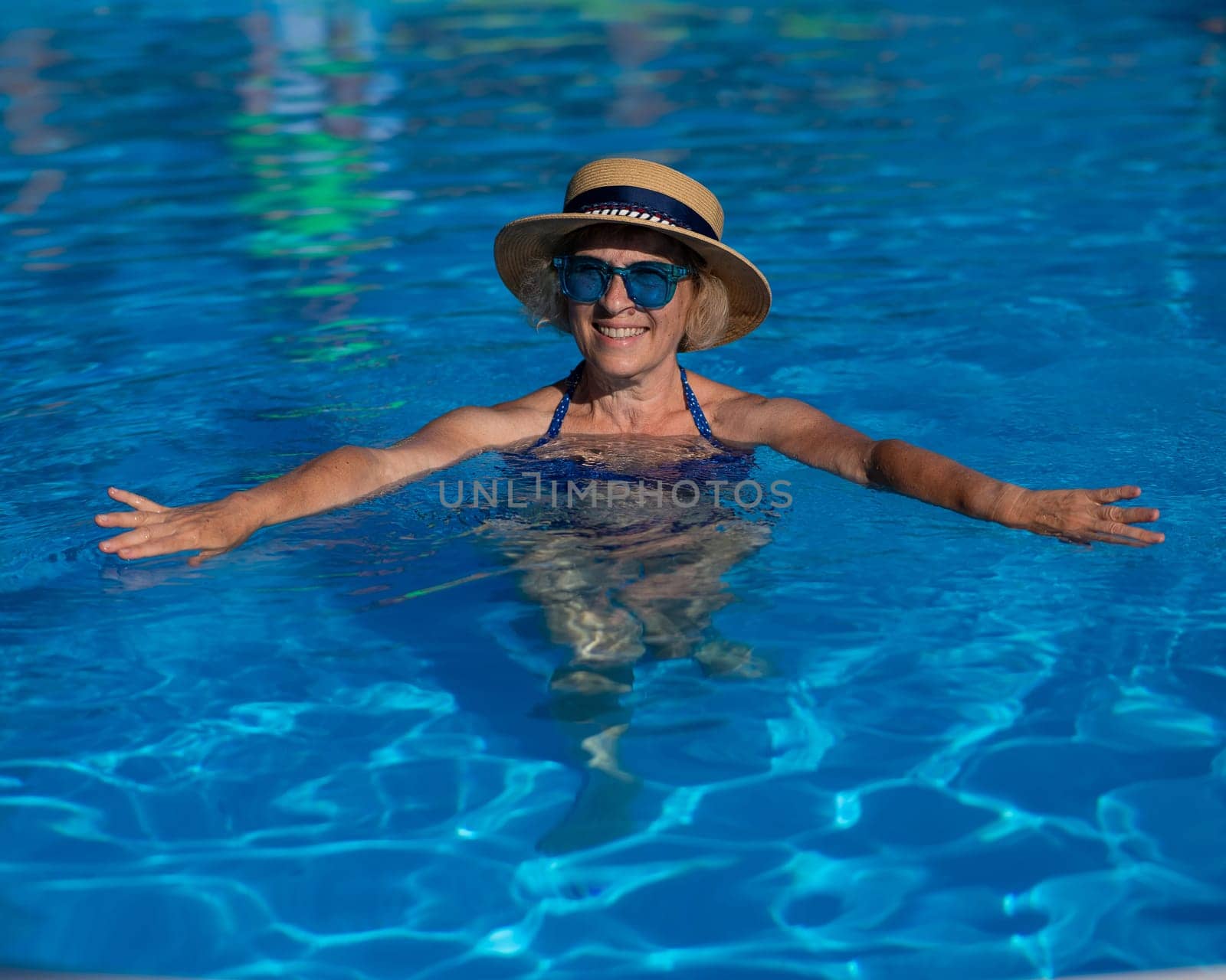 Portrait of an elderly woman in a hat and blue sunglasses swims in the pool