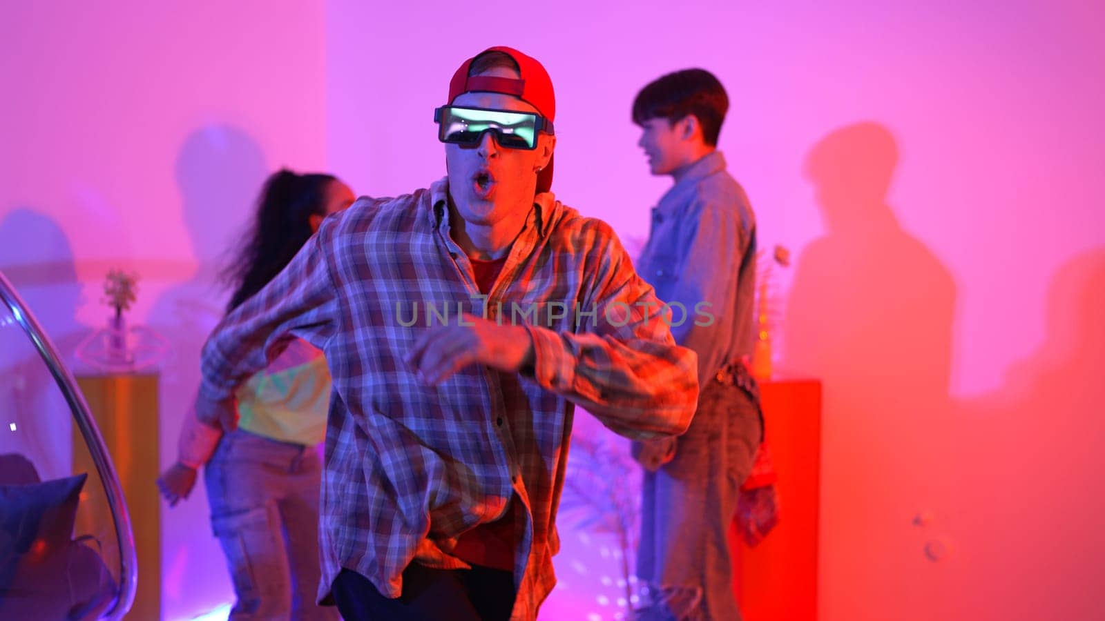Hispanic hipster wear colorful cloth and waving to freestyle music. Professional break dancer moving to lively beat with neon light and led light with modern studio surrounded by friend. Regalement.