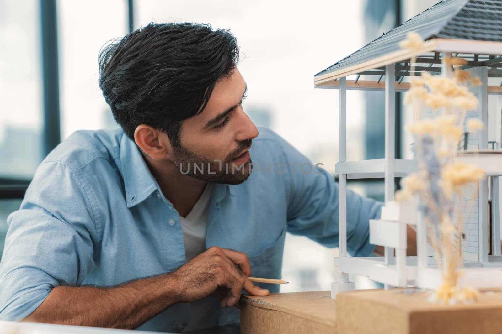 Closeup portrait of smart caucasian architect engineer inspect house model while thinking about building construction at architect studio on table with project plan, blueprint, equipment. Tracery.