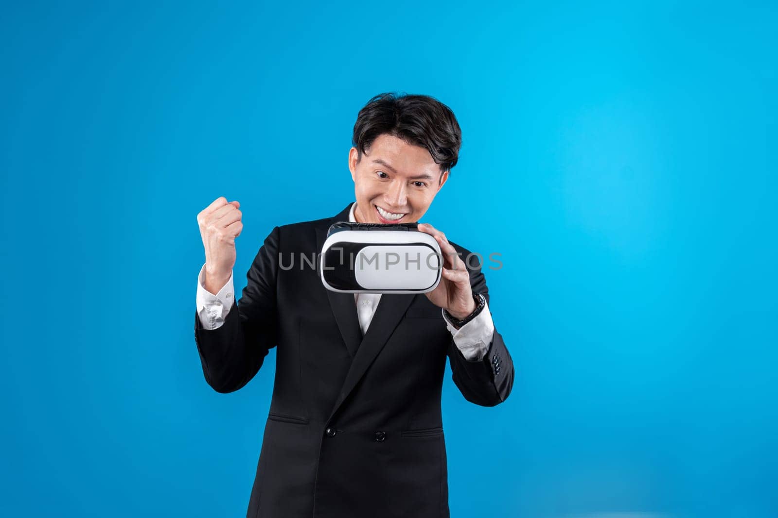 Smiling Asian businessman looking through VR connecting financial business report futuristic metaverse data analytics power bi technology virtual reality meta isolated blue copyspace. Contrivance.
