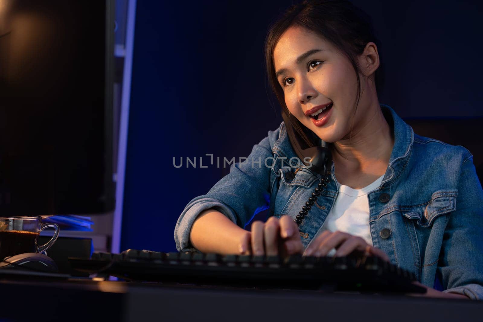 Young beautiful Asian creative woman calling on phone desk to customer or coworker explaining creator project's high profit while searching market analysis on pc at neon office at night. Stratagem.