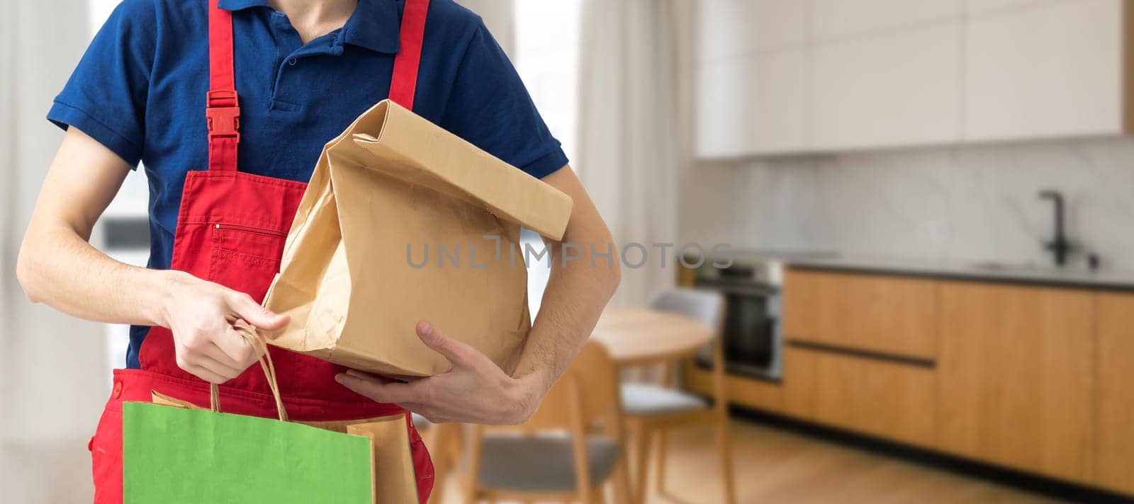 Courier holding paper bags with food, space for text. Delivery service.