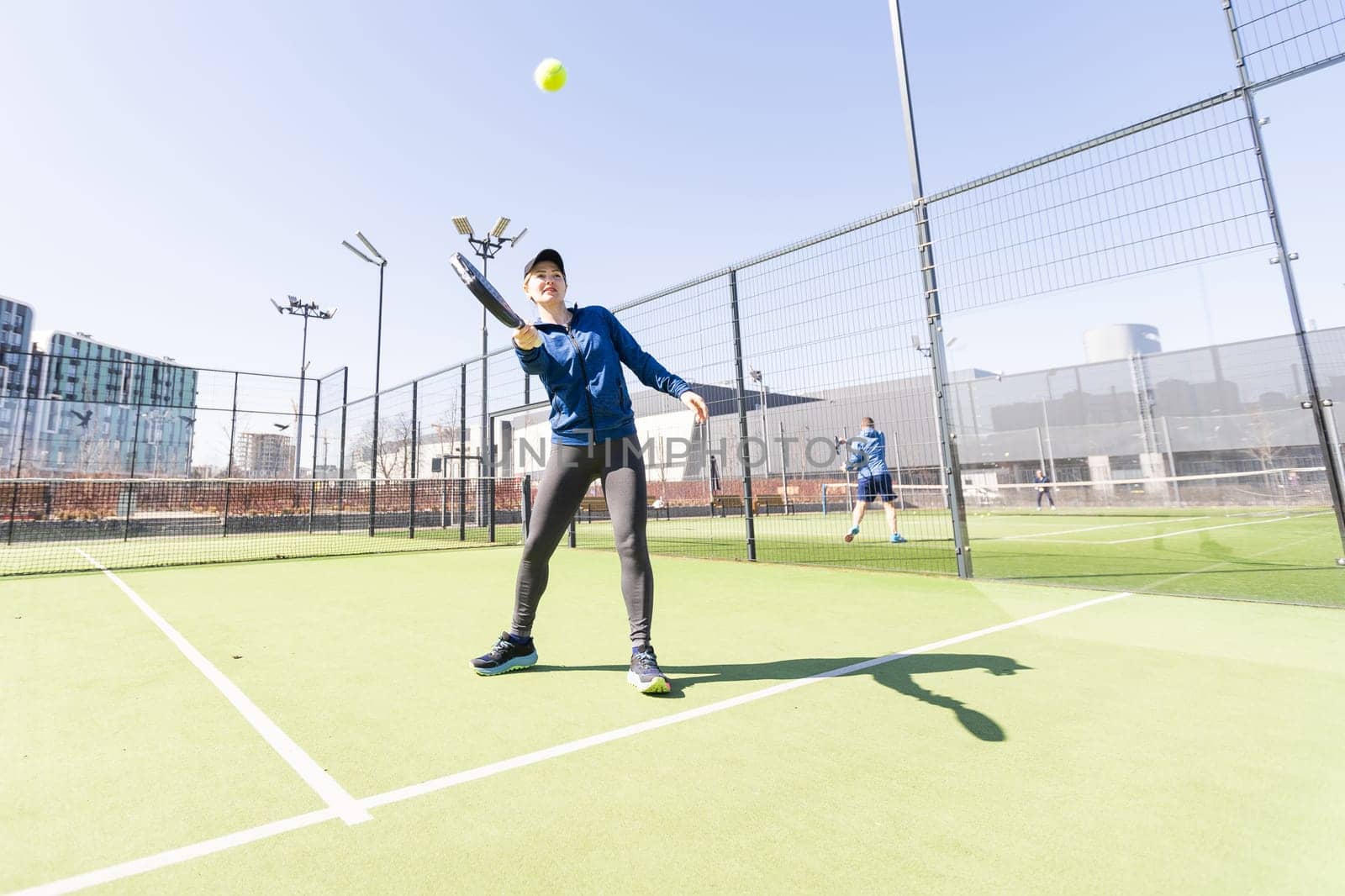 A girl in sportswear is training on a paddle tennis court. The girl is hitting the ball against the glass to make a rebound. Concept of women playing paddle. High quality photo