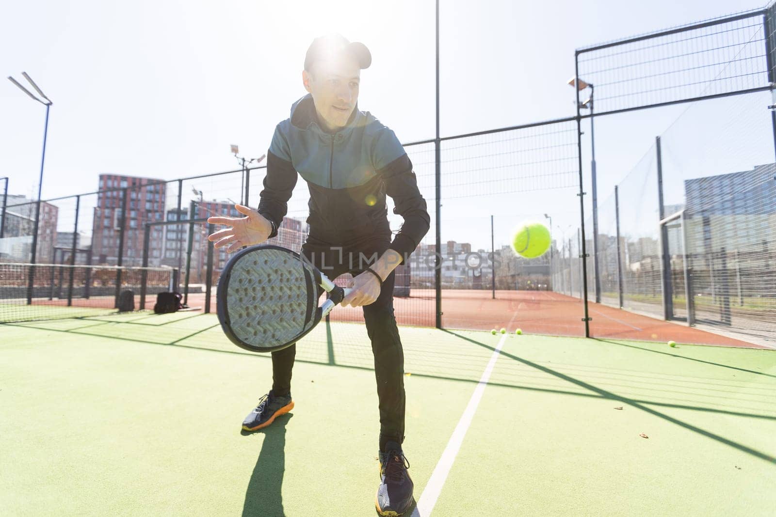 A padel player jump to the ball, good looking for posts and poster. Man with black racket playing a match in the open behind the net court outdoors. Professional sport concept with space for text. High quality photo