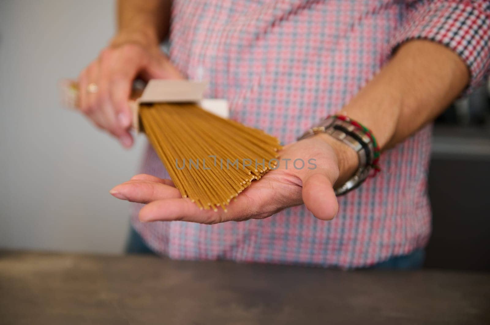 Close-up male hands holding a cardboard pack with integral spaghetti, standing at kitchen counter at home, preparing traditional Italian pasta for family dinner. Healthy food concept