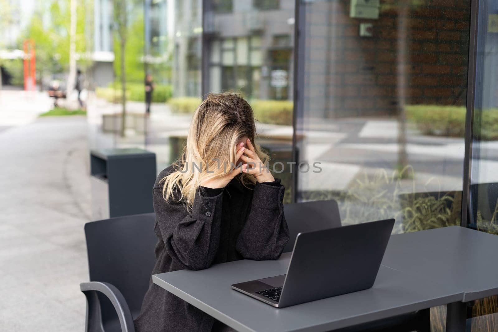 Tired young business woman in black suit with headphones is sitting with eyes closed in front of laptop by Andelov13