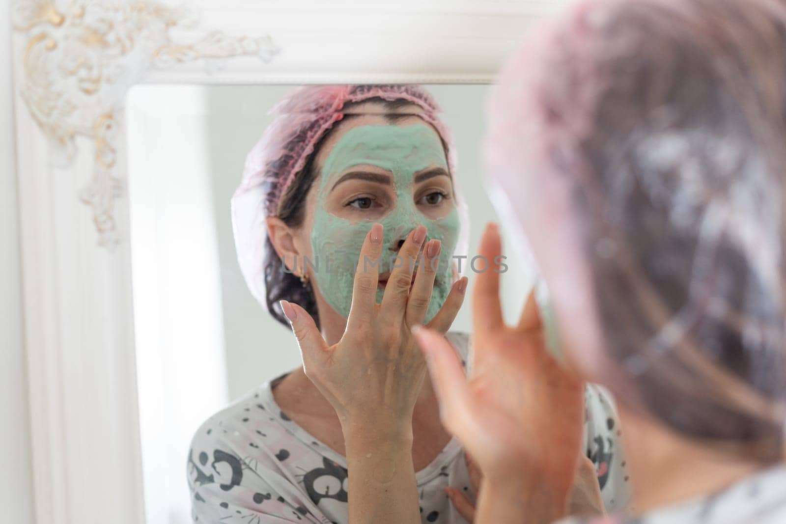 Self care: a woman applying clay mask to her face by Andelov13