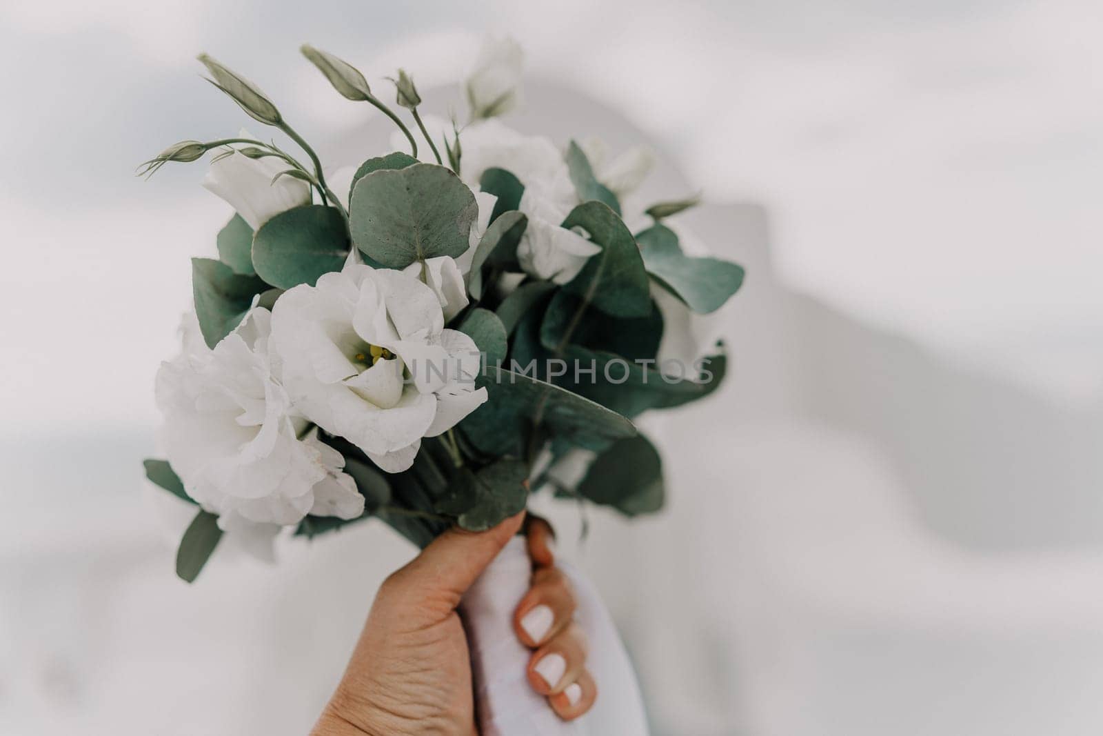 A bouquet of white flowers with green leaves is being held by a person's hand. The arrangement is simple and elegant, with the white flowers providing a clean and fresh look. by Matiunina