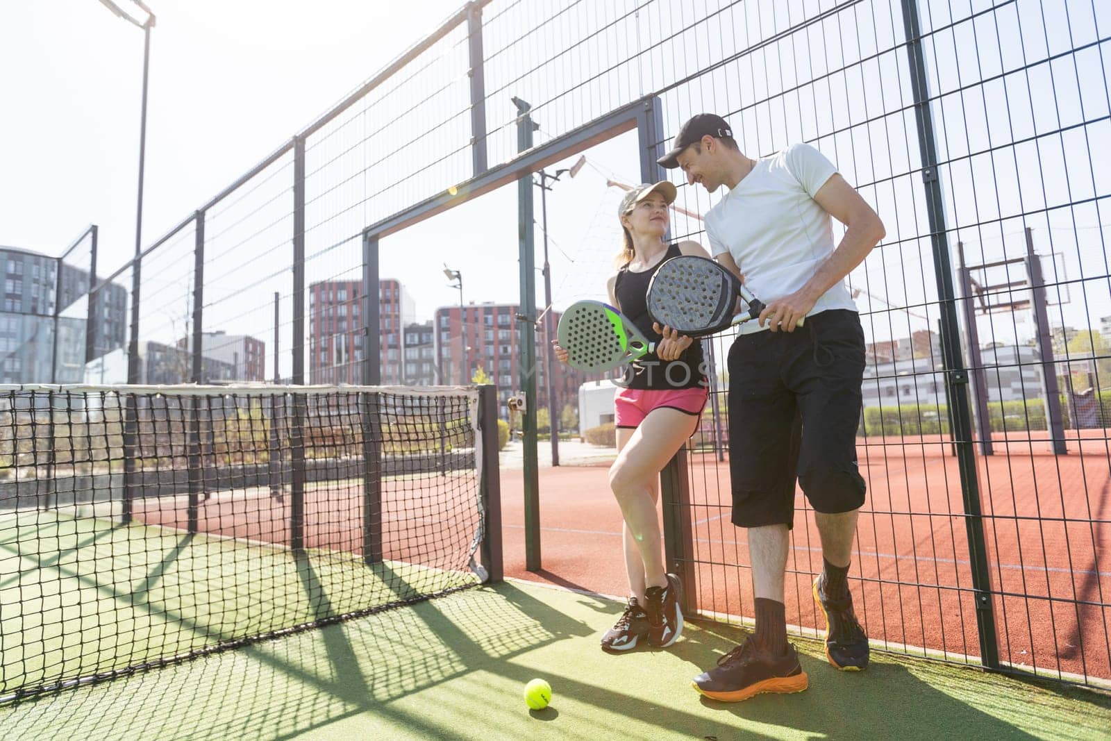 Cheerful athletic couple laughing during padel tennis match on outdoor court. High quality photo