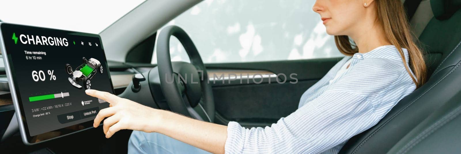 Young woman inside the vehicle, checking EV vehicle's application on battery recharging electricity status display on smart monitor screen in modern EV car on her road trip journey. Exalt