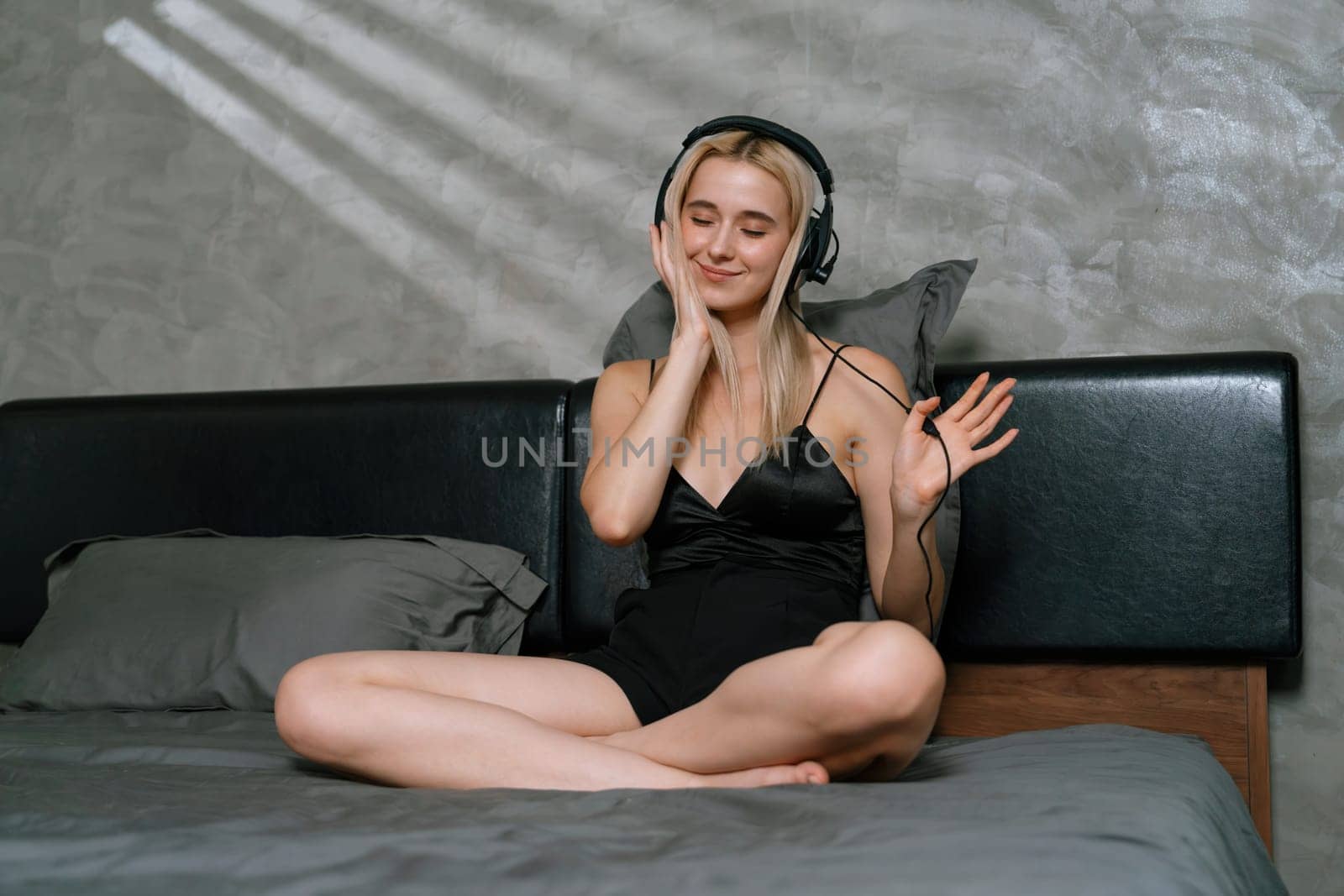 Young woman listening to music on headphone and enjoying meditative isolation on her bed with songs and, promoting a healthy lifestyle and relaxation with musical meditation. Blithe