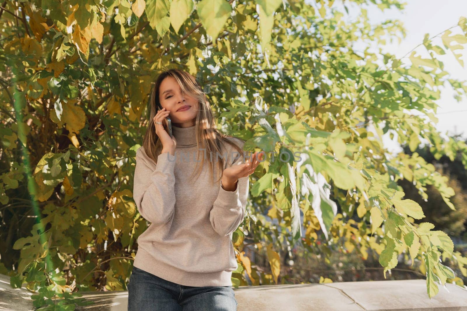 A woman is talking on her cell phone while sitting under a tree. She is smiling and she is enjoying her conversation