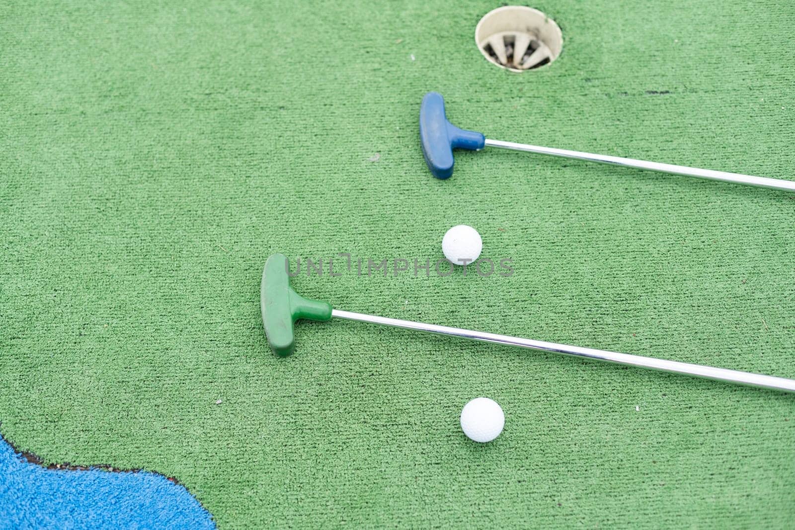 Mini-golf clubs and balls of different colors laid on artificial grass. High quality photo