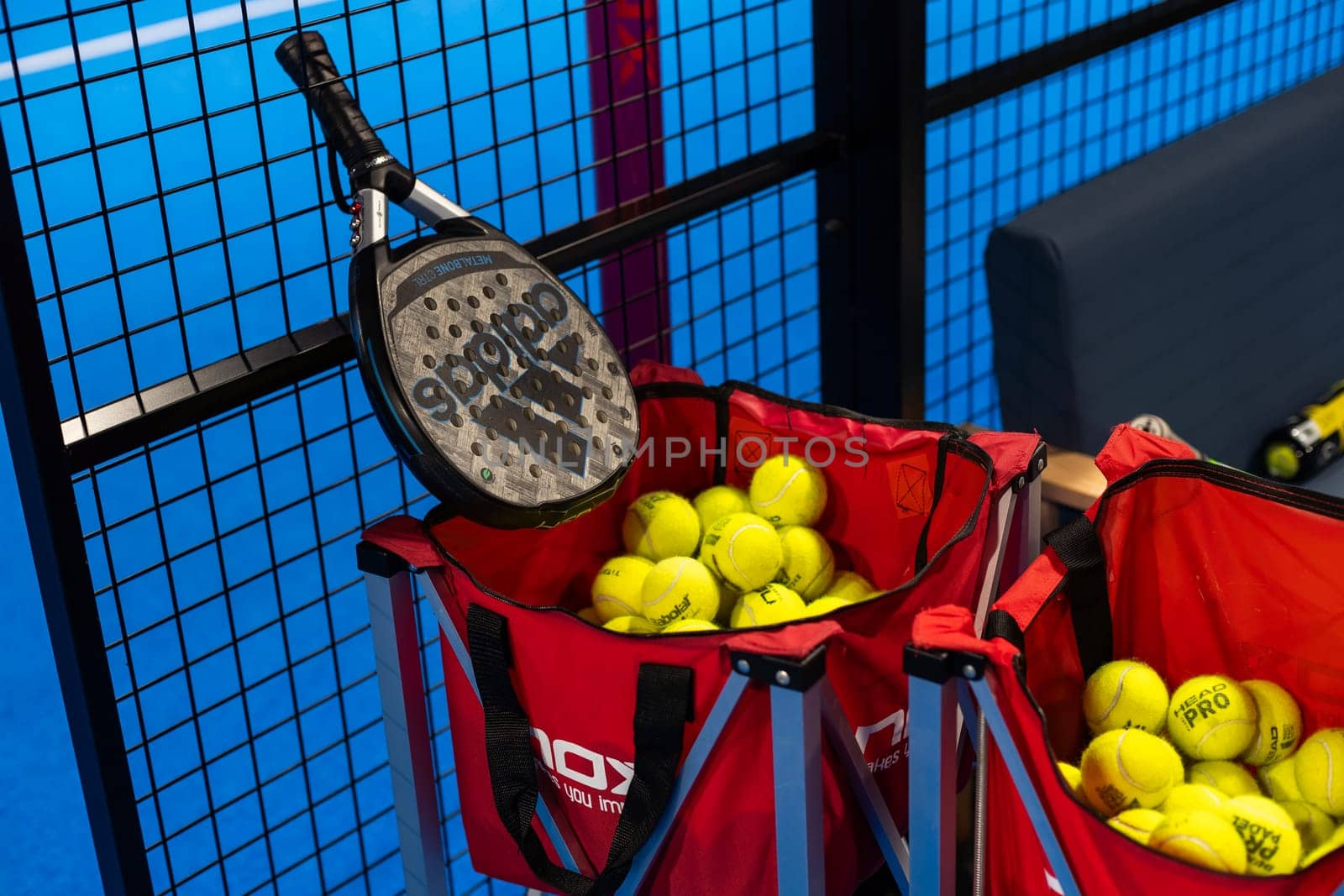 Kyiv, Ukraine, April 18, 2024. Black professional paddle tennis racket and ball with natural lighting on blue background. Horizontal sport theme poster, greeting cards, headers, website and app. High quality photo