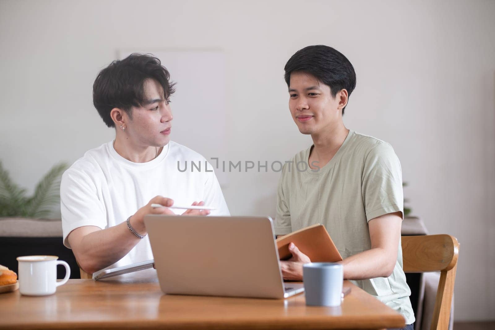 A male lgbt couple is studying together while studying online at home to prepare for an online exam. by wichayada