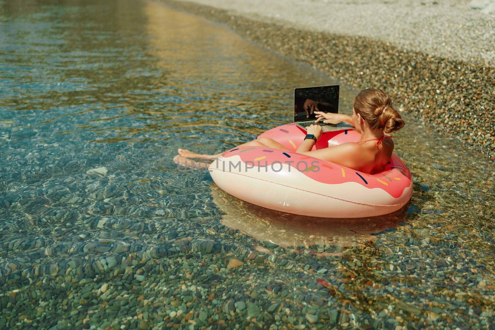 Woman laptop sea. Freelancer woman in sunglases floating on an inflatable big pink donut with a laptop in the sea. People summer vacation rest lifestyle concept