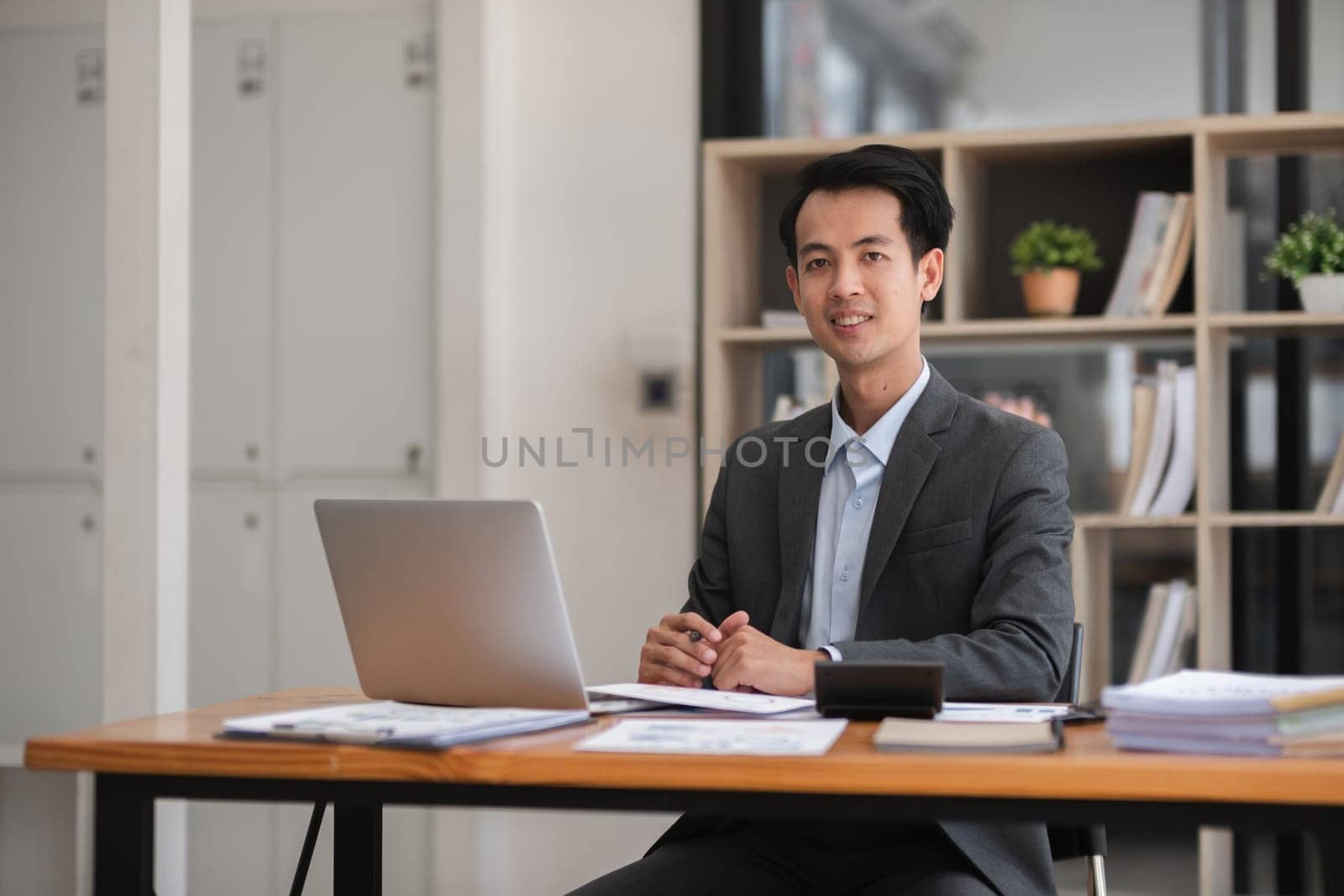 Young Asian businessman working using laptop in modern office, analyzing accounts Financial investment information report.