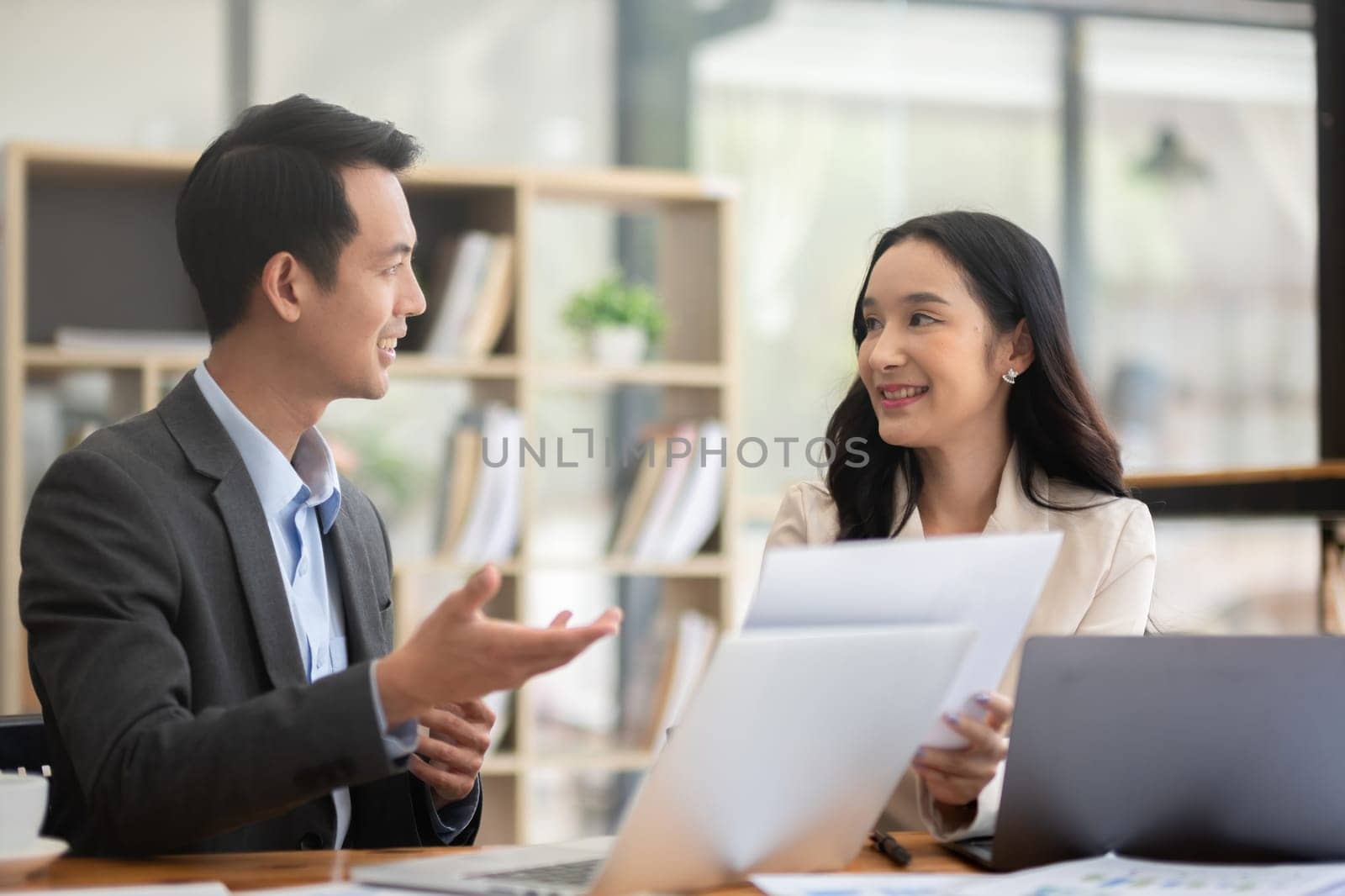A young businessman and a female Asian accountant are discussing financial accounting and business planning together in the office. by wichayada
