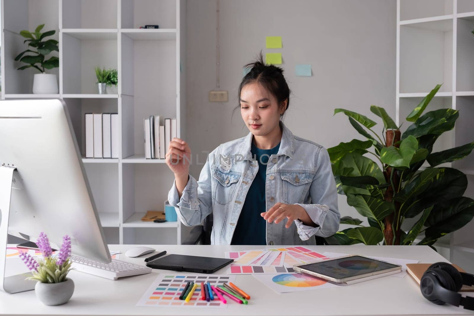 Female designer working in graphic design Choose colors for graphic design work. Focused work on a table full of colored paper for working on a computer by wichayada