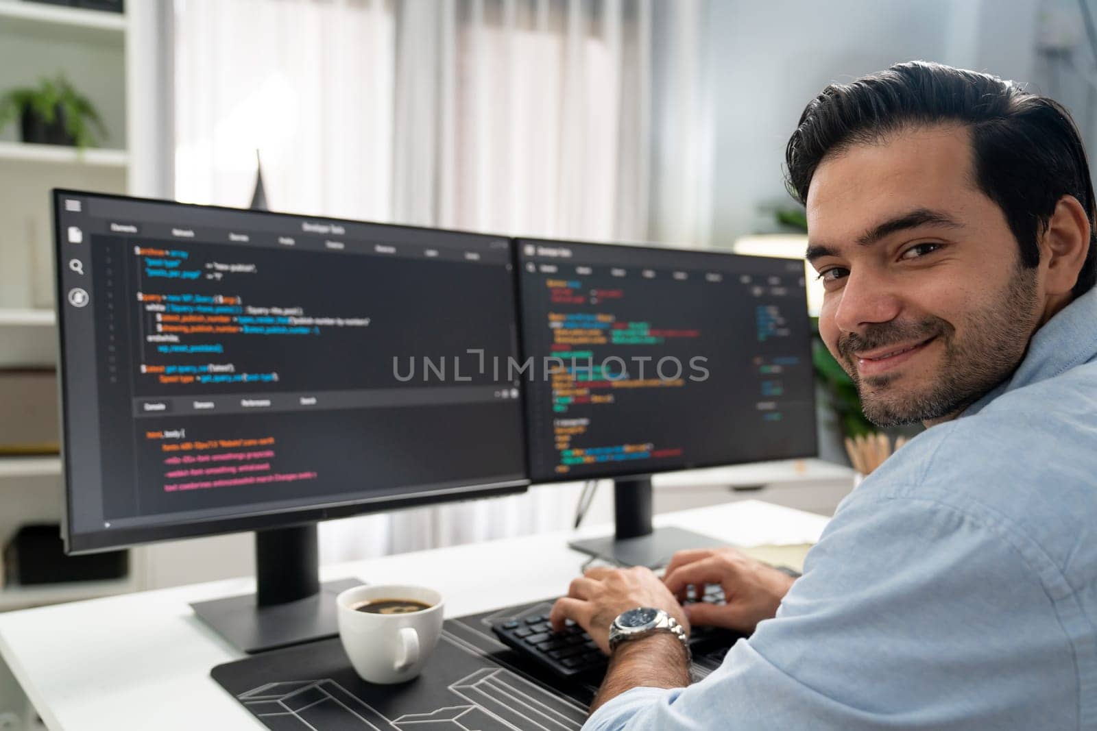 Smiling smart IT developer working software development looking camera with coding on two pc creating virus firmware application program version on website with coffee cup at modern office. Surmise.