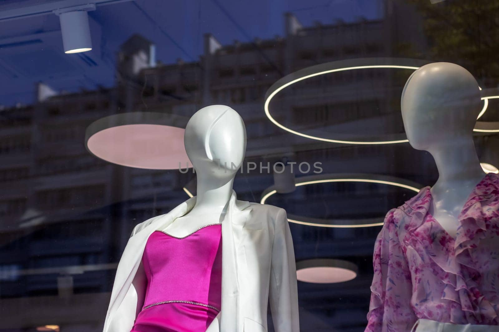 Two mannequins in a retail store window are showcased wearing fun pink dresses and stylish eyewear. The fashion design event features magenta headgear for a touch of whimsy and leisure