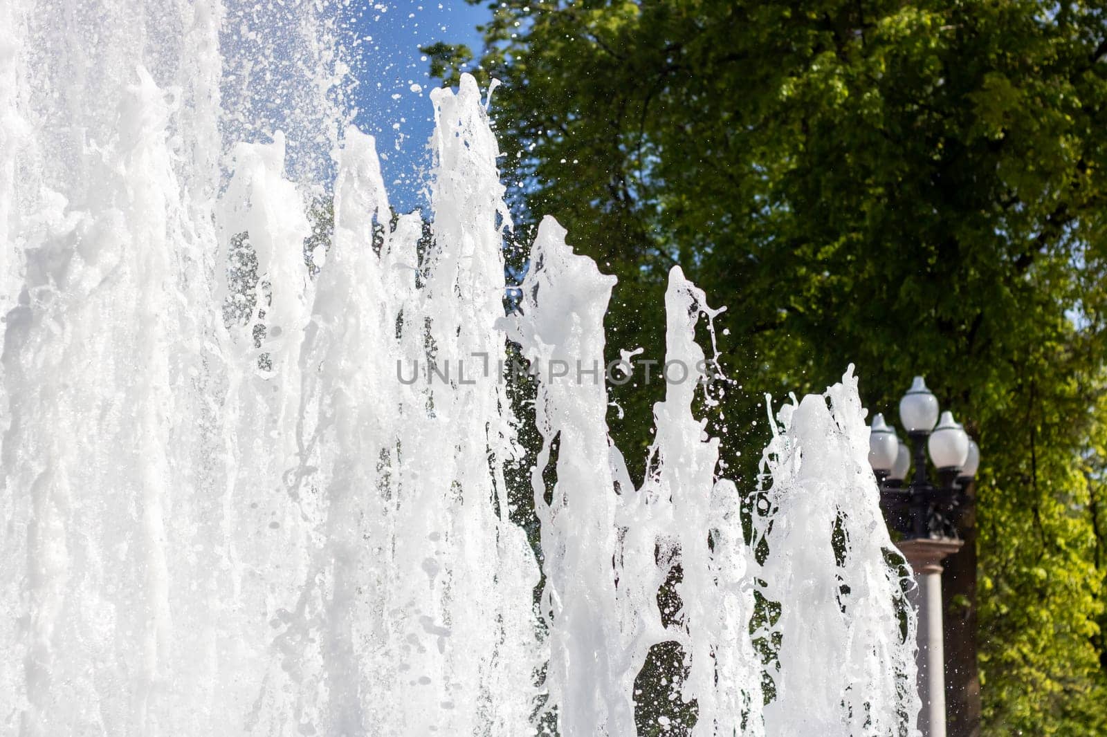 A fountain in a park with trees in the background, the flowing water creating a serene atmosphere amidst the greenery. The liquid flows freely, creating a calming watercourse