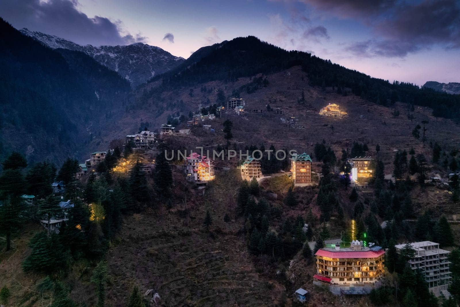 aerial drone landing shot showing lit multi floor story buildings on side of hill at night evening showing hotels shopping areas in manali, shimla himachal India