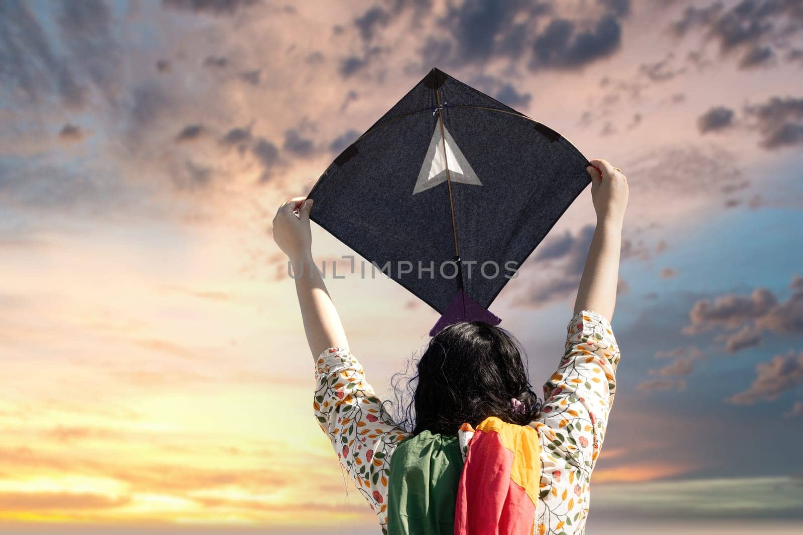 Young girl in traditional indian clothing holding black kite high above head launching it on sankranti republic independence day celebrations