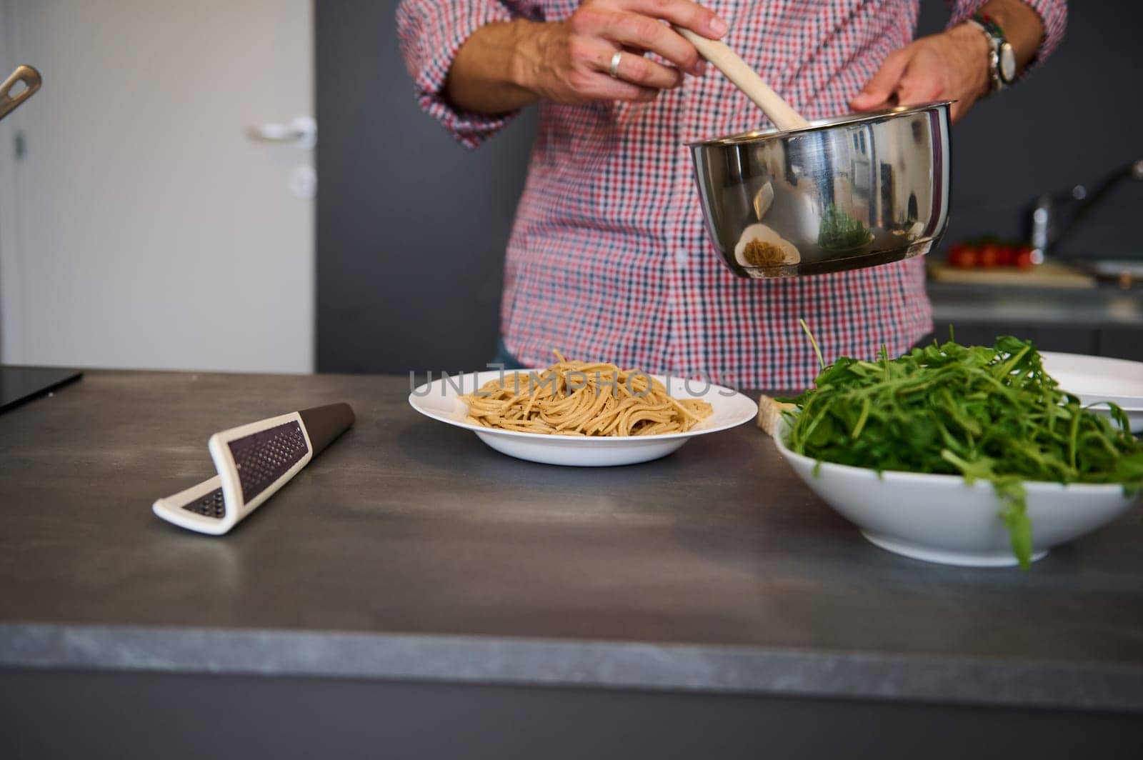 Cropped image of a chef pouring tomato sauce on Italian pasta, plating up the dish before serving. Man cooking dinner at home kitchen. Cuisine. Culinary. Epicure. Italian traditional food concept