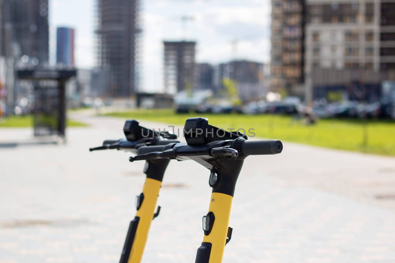 A black and yellow scooter with an electric blue bicycle handlebar is parked on the side of the asphalt road in the city, blending in with the metal car passing by. A vehicle for recreation