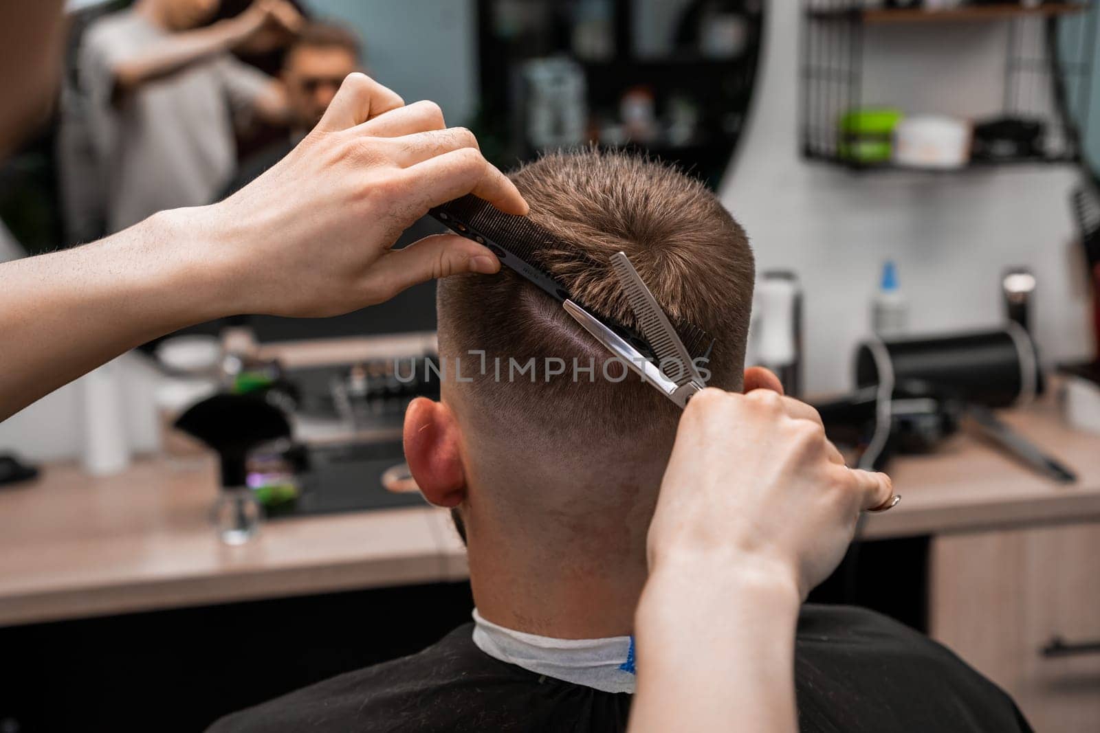 Barber using scissors and comb styling man hair at the barbershop