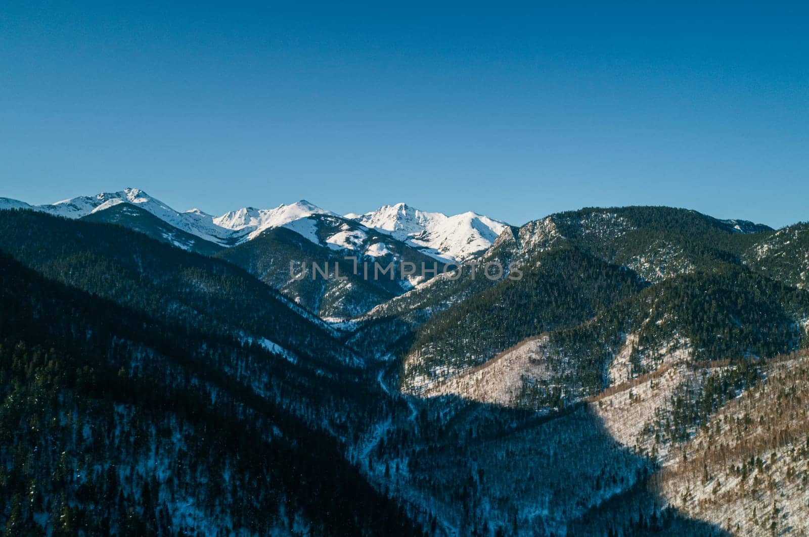 Aerial landscape mountains covered with forest and snow-capped peaks in the background. Cinematic winter mountains landscape
